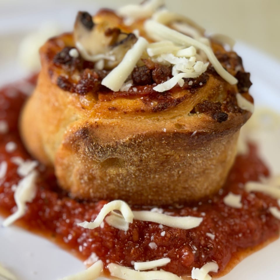 Savory pizza roll with mushrooms, sausage, and shredded cheese, served on a bed of marinara sauce.