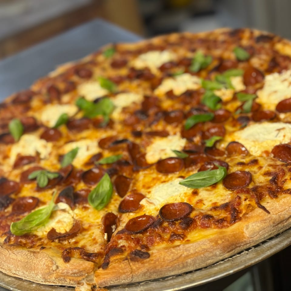 A freshly baked pizza with pepperoni, melted cheese, and basil leaves on a metal pan.