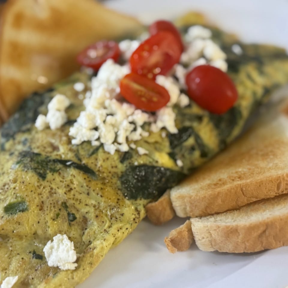 Spinach omelet topped with feta cheese and cherry tomatoes, served with toast.