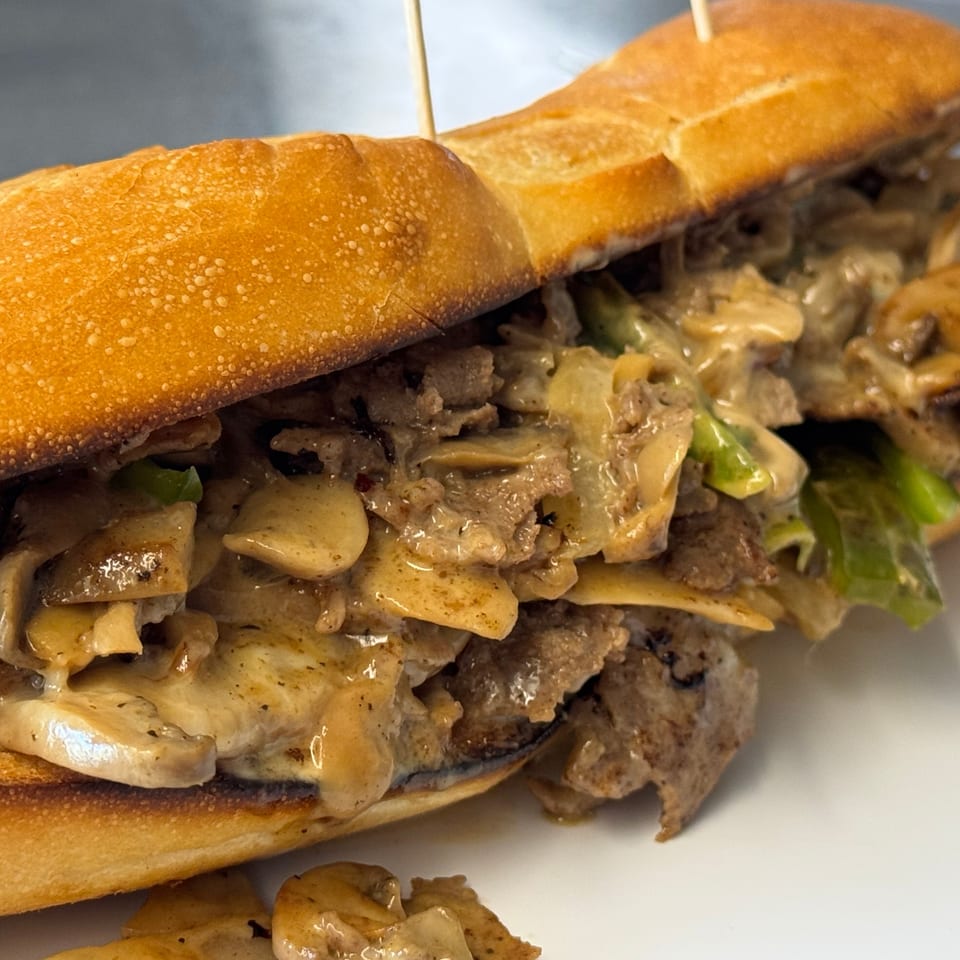 Cheesesteak sandwich with steak, mushrooms, onions, and green peppers on a toasted hoagie roll.