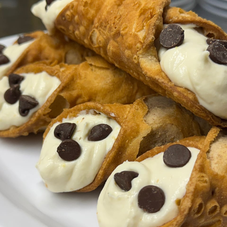 A close-up of several golden-brown cannoli filled with white cream and chocolate chips.