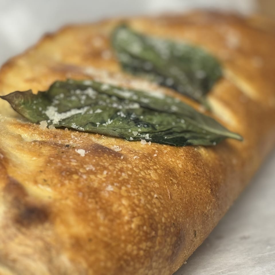 Golden-brown calzone topped with fresh basil leaves and sprinkled with coarse salt.